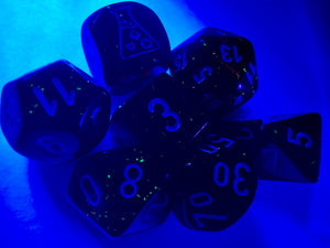 Borealis Luminary Blood Orange polyhedral set, showing off brilliant sparkly orange dice, glowing under a black light.