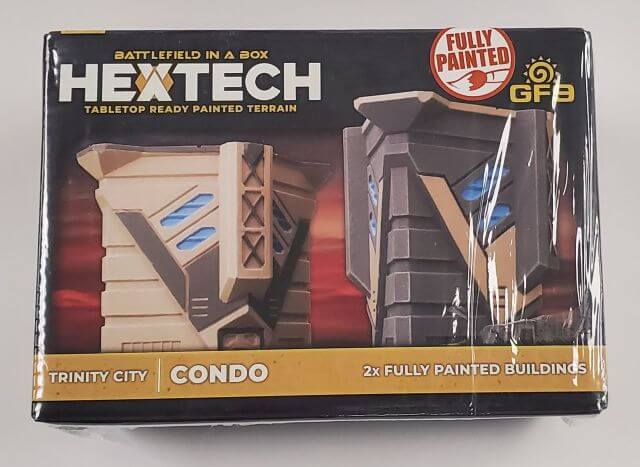 Packaged BattleTech Hextech terrain piece depicting a condominium building with a pre-painted blue and gray facade, labeled as 'Trinity City - Condo', indicating it comes with two fully painted buildings.