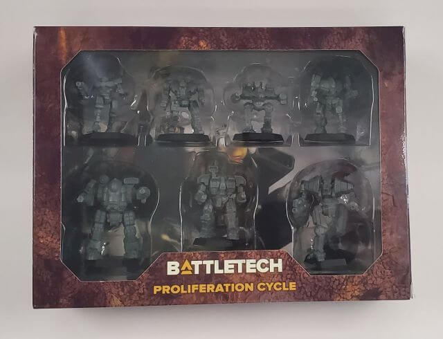 A box of BattleTech miniatures game containing seven assembled mechs in gray, along with pilot and Alpha Strike cards.