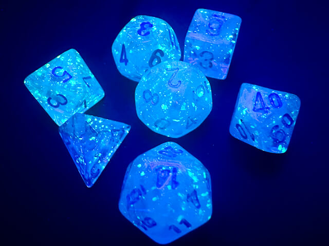 A close of the Chessex  Luminary Sky mini dice set under black light highlighting the glow in the dark nature of the dice.