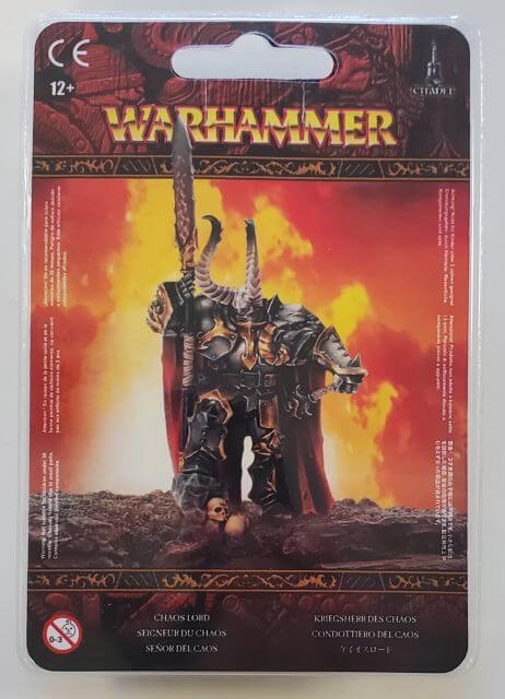 Packaging for Warhammer Slaves to Darkness Chaos Lord miniature, featuring the figure in a dramatic pose with a sword, with a red and orange fiery background.