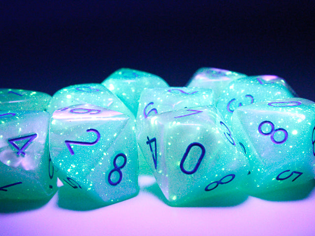 Close up of the Gemini Pearl Turquoise-White with blue 10 d10 dice set under black light to highlight their luminescent qualities. 