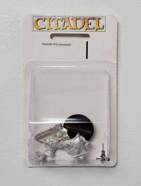 A packaged metal miniature figurine named 'Preacher with Chainsword' from the Adeptus Sororitas line, displayed in plastic blister packaging.