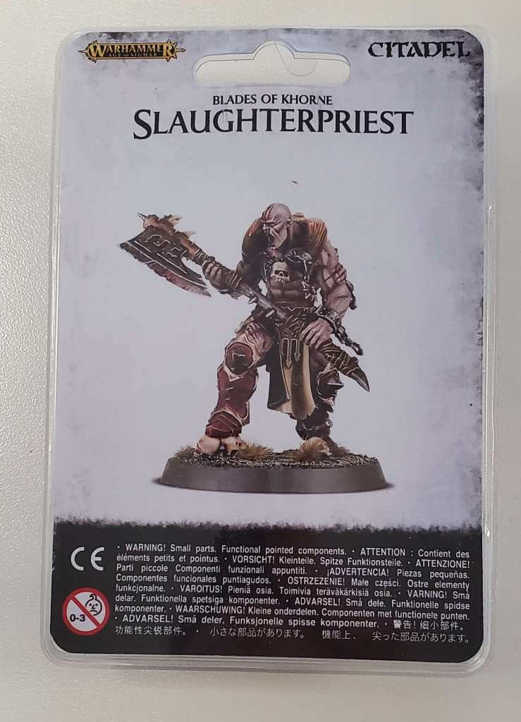 Packaged miniature figure named 'Blades of Khorne Slaughterpriest' on a plastic card, showing the character equipped with a large axe and bone mutations.