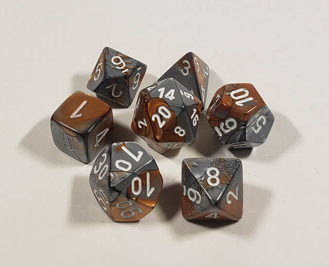 A close up of the Chessex Gemini Copper and Steel polyhedral dice set.