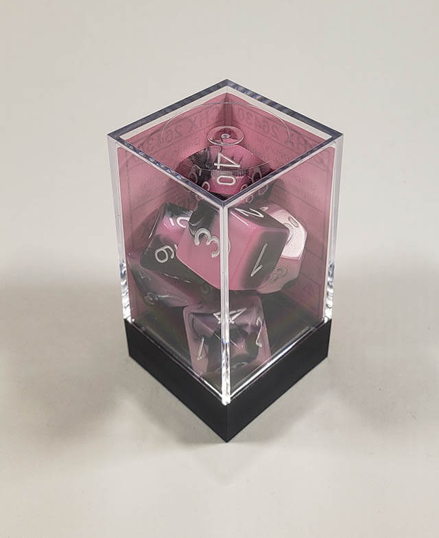 A close up of the Chessex Gemini Black and Pink polyhedral dice set in its package.
