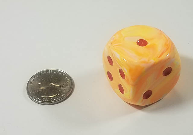 A swirled orange and yellow dice with red spots next to a quarter for size comparison.