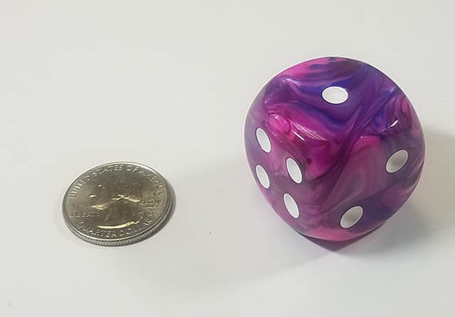 A swirled pink and purle dice with white spots next to a quarter for size comparison.