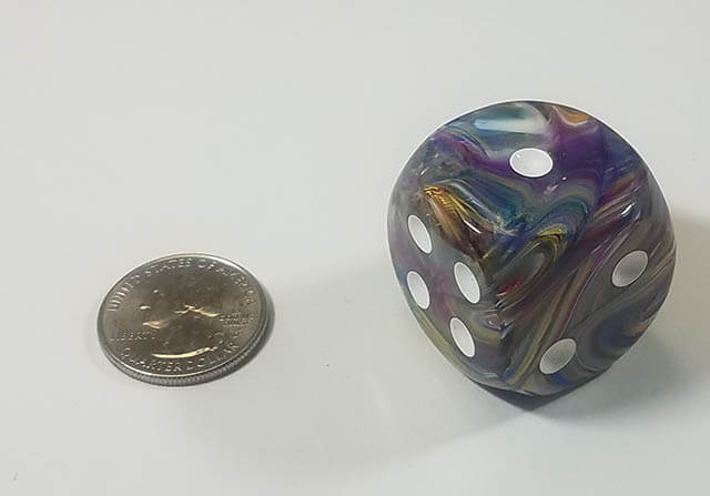 A multicolored, round dice with white pips, alongside a quarter for scale, suggesting the size of the dice.