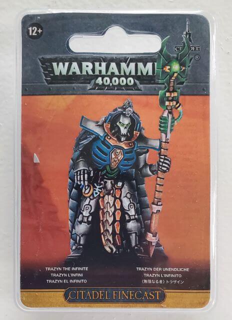 Packaging for Warhammer 40,000 figure Trazyn the Infinite, featuring a resin cast kit on a card with the figure depicted in black, blue, and green armor holding a staff.
