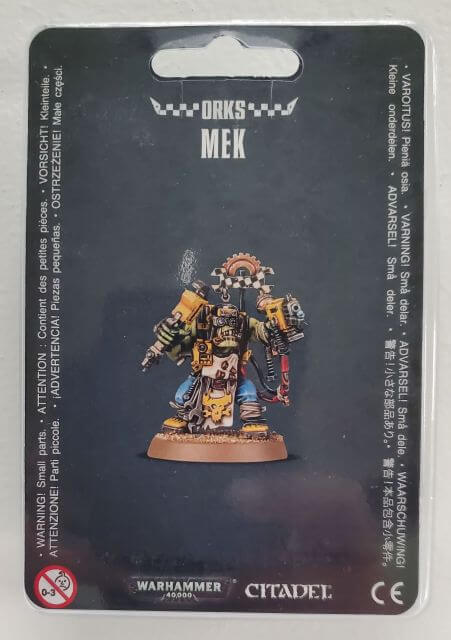 Packaged Ork Mek miniature on a card, with a kustom mega slugga and tools, mounted on a 32 mm round base.